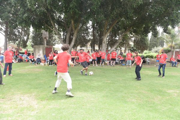 קבוצת אנשים עומדת ומשחקת כדורגל על מגרש דשא בחולצות אדומות