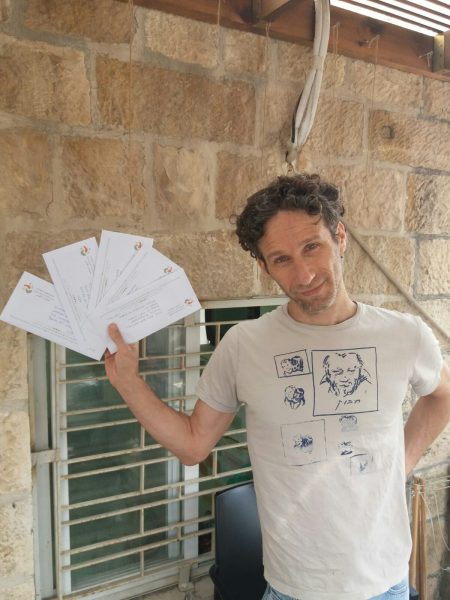 גבר עומד ומחזיק חפיסת קלפים בידו ברקע בית מאבנים ירושלמי קלאבהאוס ירושלים
