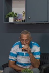 גבר יושב במרכז התמונה עם כוס קפה ביד קלאבהאוס טבריה
