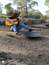 אישה יושבת ונגנת בגיטרה לצד סאג' קלאבהאוס טבריה