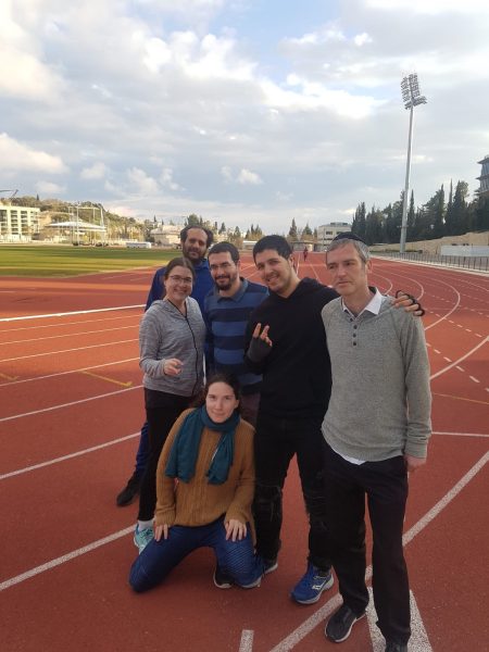 6 אנשים בתמונה קבוצתית ברקע מגרש ריצה ואטלתיקה. ירושלים קלאבהאוס